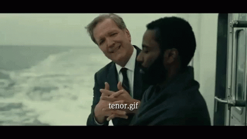 A Man In A Suit And Tie Is Talking To Another Man In A Black Shirt . GIF