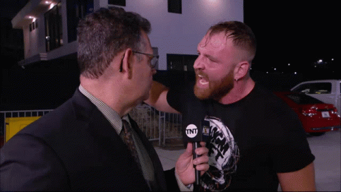 A Man In A Suit And Tie Is Talking To Another Man In A Black Shirt That Says Tnt GIF
