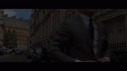 A Man In A Suit And Tie Is Talking To Another Man In A Room With A Sign In A Foreign Language GIF