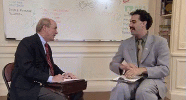 A Man In A Suit And Tie Is Talking To Another Man In Front Of A White Board GIF