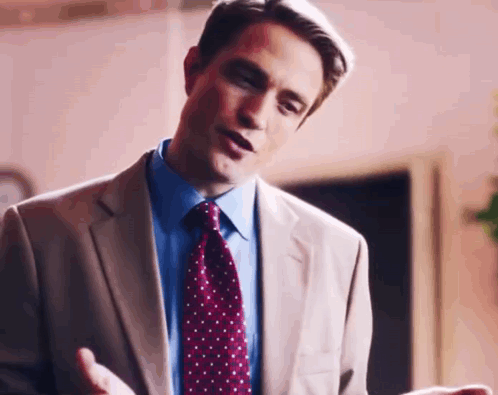 A Man In A Suit And Tie Is Talking To Someone While Standing In A Room . GIF