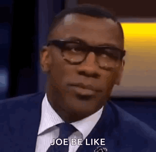 A Man In A Suit And Tie Is Talking To Someone While Wearing Glasses . GIF