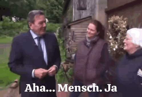 A Man In A Suit And Tie Is Talking To Two Women In Front Of A Building With The Words Aha Mensch Ja On The Bottom GIF