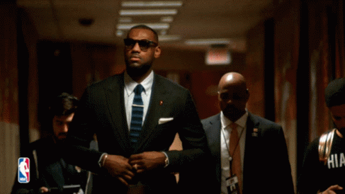 A Man In A Suit And Tie Is Walking Down A Hallway GIF