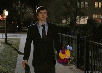 A Man In A Suit And Tie Is Walking Down A Sidewalk Holding A Bouquet Of Flowers .. GIF