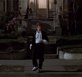 A Man In A Suit And Tie Is Walking Down A Street At Night GIF