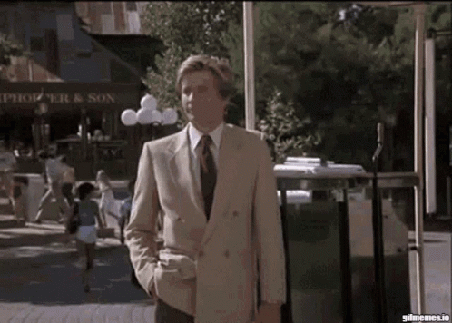A Man In A Suit And Tie Is Walking Down A Street In Front Of A Store That Says Springer & Son GIF
