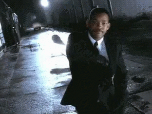A Man In A Suit And Tie Is Walking Down A Wet Sidewalk GIF