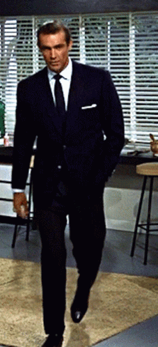 A Man In A Suit And Tie Is Walking In A Kitchen GIF