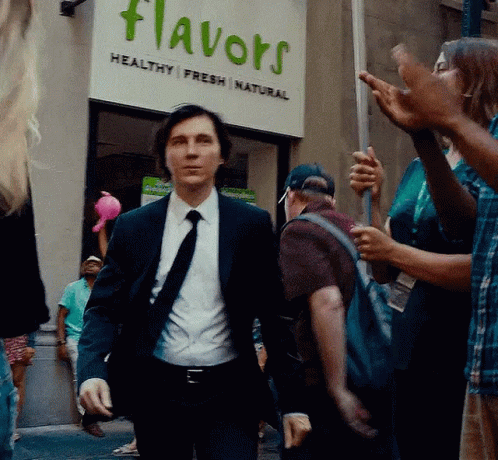 A Man In A Suit And Tie Is Walking In Front Of A Flavors Sign GIF