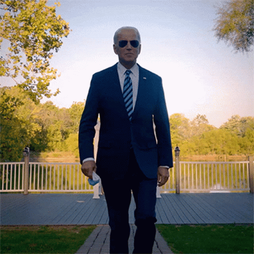 A Man In A Suit And Tie Is Walking On A Path GIF