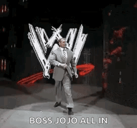 A Man In A Suit And Tie Is Walking On A Stage In Front Of A W Logo . GIF