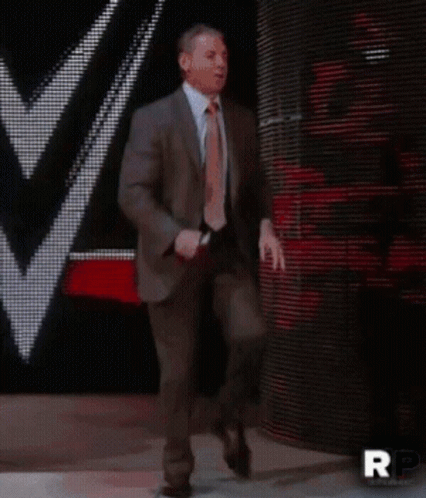 A Man In A Suit And Tie Is Walking On A Stage With Rp Written On The Bottom Right GIF
