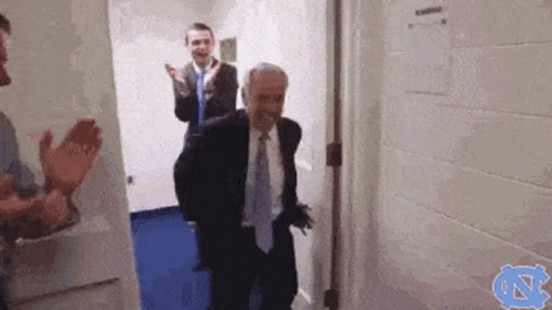 A Man In A Suit And Tie Is Walking Through A Doorway While Other Men Applaud . GIF