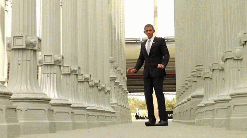 A Man In A Suit And Tie Is Walking Through Columns GIF