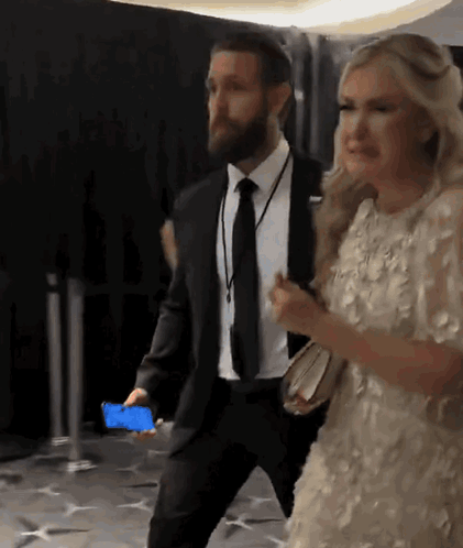 A Man In A Suit And Tie Is Walking With A Woman In A Dress GIF