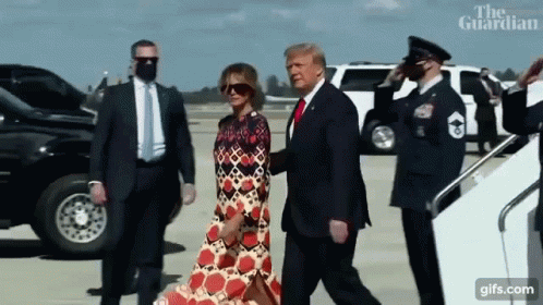 A Man In A Suit And Tie Is Walking With A Woman In A Dress .. GIF