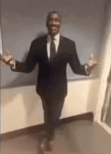 A Man In A Suit And Tie Is Walking With His Arms Outstretched . GIF