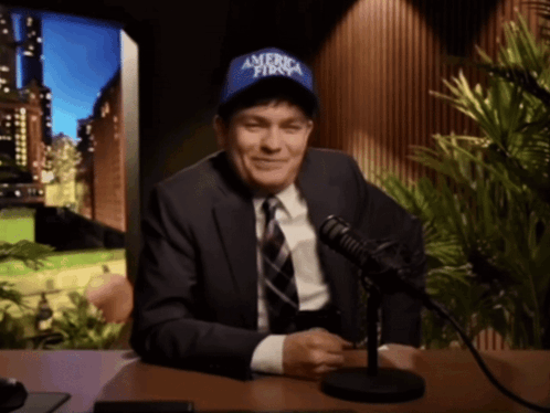 A Man In A Suit And Tie Is Wearing A Blue Hat That Says America First GIF