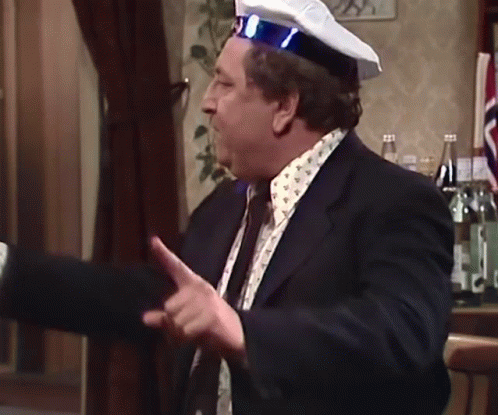A Man In A Suit And Tie Is Wearing A Captain 'S Hat GIF