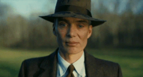 A Man In A Suit And Tie Is Wearing A Fedora Hat . GIF