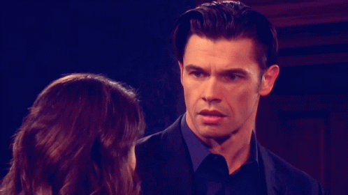 A Man In A Suit And Tie Looks At A Woman GIF
