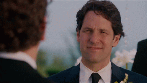 A Man In A Suit And Tie Looks At Another Man In A Black Suit GIF