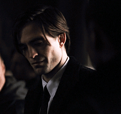 A Man In A Suit And Tie Looks At The Camera In A Dark Room GIF