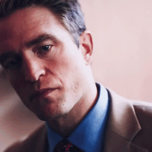 A Man In A Suit And Tie Looks At The Camera With A Serious Look On His Face GIF