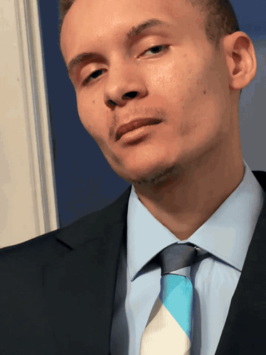 A Man In A Suit And Tie Looks At The Camera With His Eyes Closed GIF