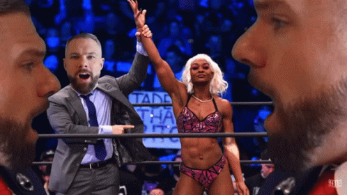 A Man In A Suit And Tie Points At A Woman In A Bikini In A Wrestling Ring GIF