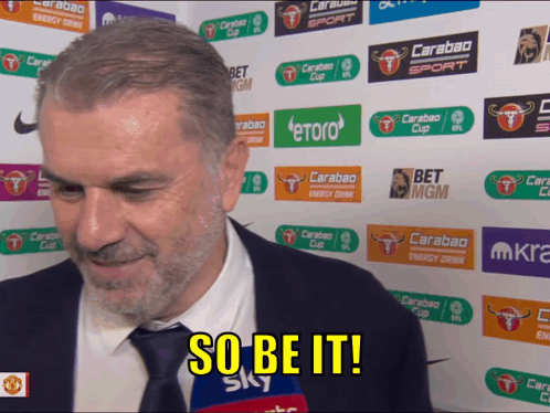 A Man In A Suit And Tie Says So Be It In Front Of A Wall Of Advertisements GIF