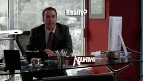 A Man In A Suit And Tie Sits At A Desk With A Sign On It That Says ' Really ? ' GIF