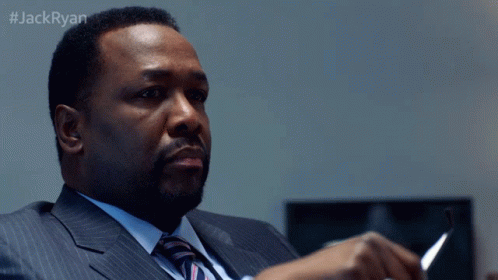 A Man In A Suit And Tie Sits At A Desk With The Hashtag #Jackryan On The Bottom GIF