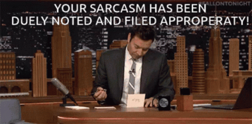 A Man In A Suit And Tie Sits At A Desk With The Words Your Sarcasm Has Been Duly Noted And Filed GIF