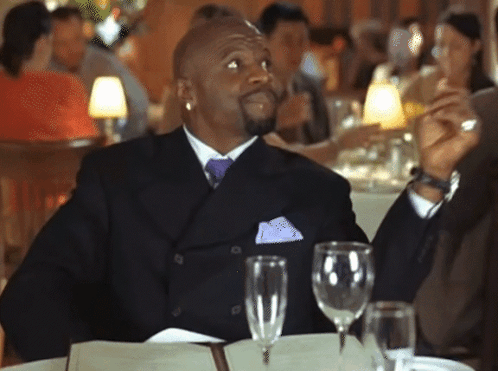 A Man In A Suit And Tie Sits At A Table With Wine Glasses And A Menu GIF