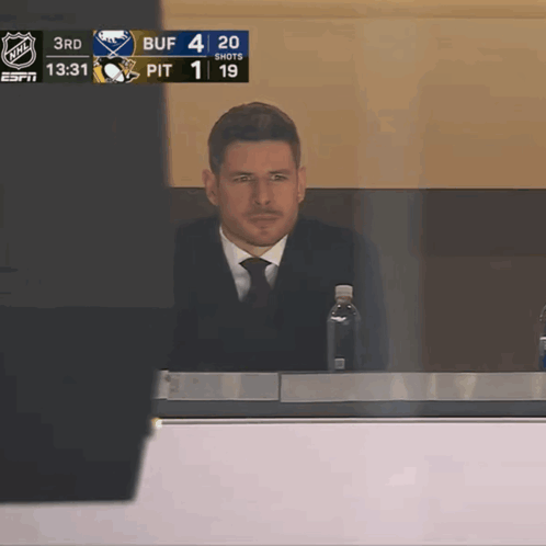 A Man In A Suit And Tie Sits In A Broadcast Booth With A Bottle Of Water GIF