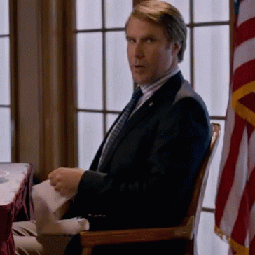 A Man In A Suit And Tie Sits In A Chair GIF