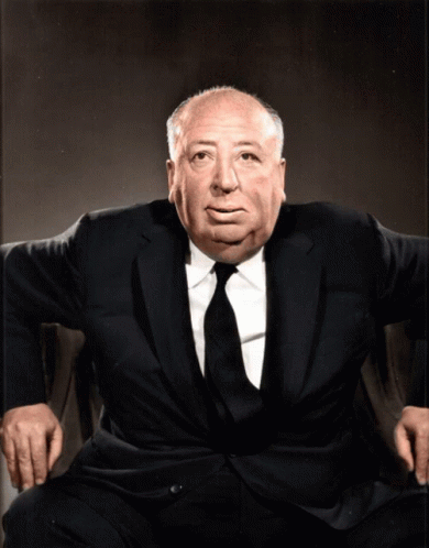 A Man In A Suit And Tie Sits In A Chair With His Hands On His Knees GIF