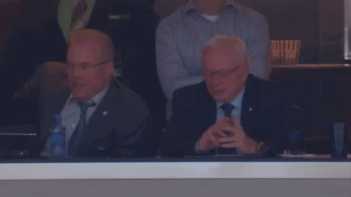 A Man In A Suit And Tie Sits In A Stadium Watching A Game GIF