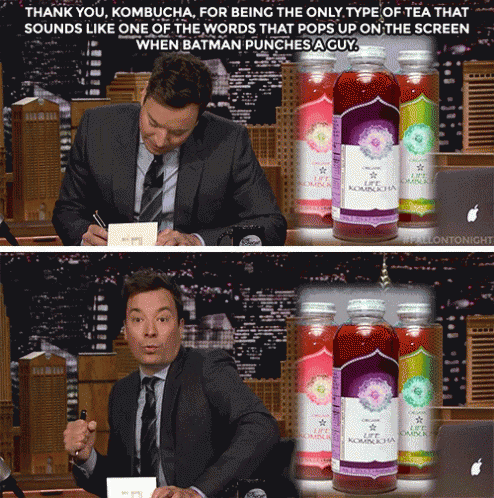 A Man In A Suit And Tie Sits In Front Of A Bottle Of Kombucha GIF