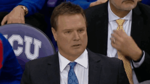A Man In A Suit And Tie Sits In Front Of A Seat That Says Cu On It GIF