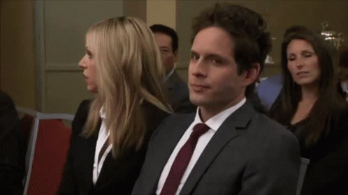 A Man In A Suit And Tie Sits Next To A Woman In A Black Suit GIF