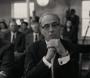 A Man In A Suit And Tie Sits With His Hands Folded In Front Of Him GIF