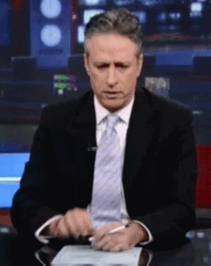 A Man In A Suit And Tie Sitting At A Desk GIF