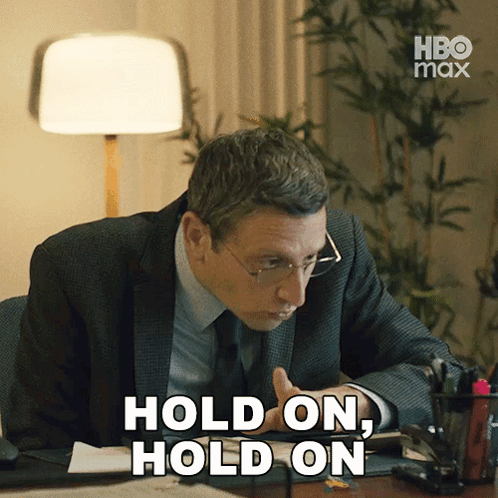 A Man In A Suit And Tie Sitting At A Desk With The Words Hold On Hold On GIF