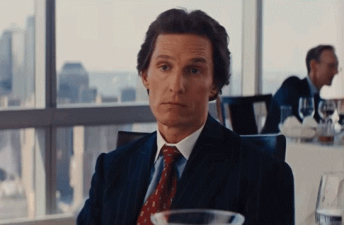 A Man In A Suit And Tie Sitting At A Table GIF