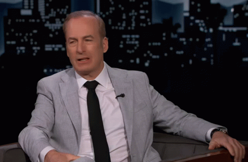 A Man In A Suit And Tie Sitting In A Chair GIF