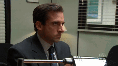 A Man In A Suit And Tie Sitting In Front Of A Nbc Logo GIF