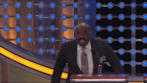 A Man In A Suit And Tie Stands At A Podium With A Microphone GIF
